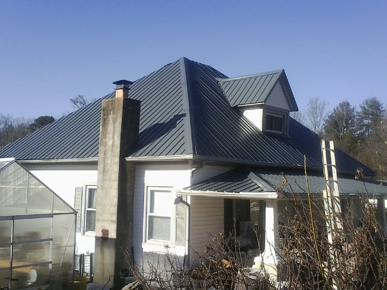 Dark blue standing seam metal roof on a white farmhouse with dormer — Slate & Tile Roof Repair by Roofing Brothers in Sterling