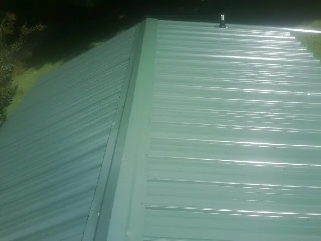 New green metal panels meeting at the ridge of a roof — Flat Roof Repair work by our crew in Sterling