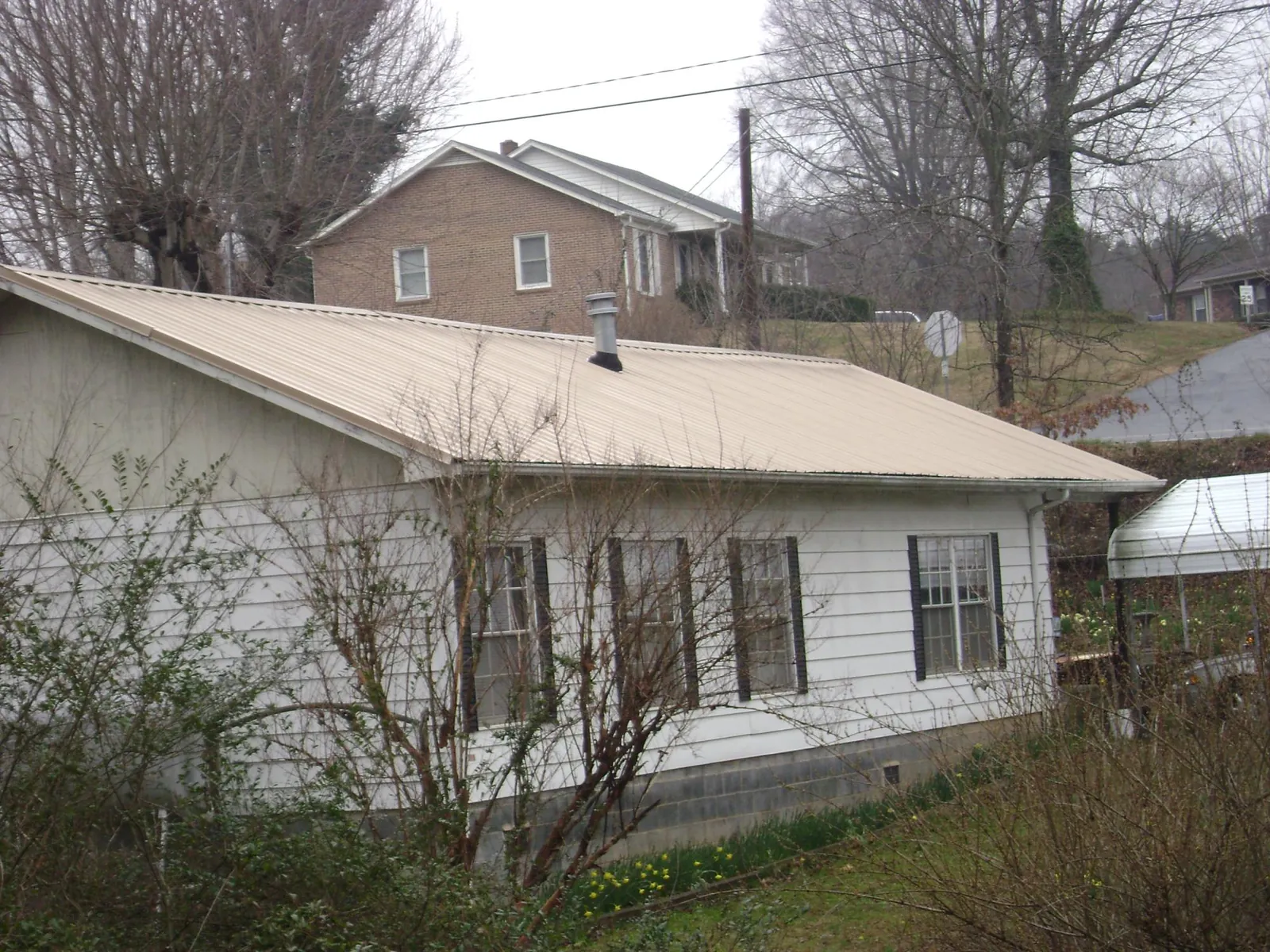 Tan metal roof on a white sided house set into a hillside — Commercial Roofing by Roofing Brothers in Sterling